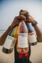 Friends holding Amabile di Rosa bottles on the beach at sunset